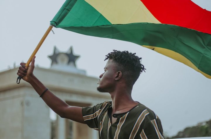 african-male-with-dreadlocks-raising-flag-of-ghana-country-with-colorful-stripes-while-looking-away-1