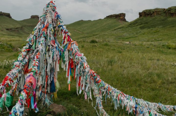 tibetan-bright-flags-located-in-field-with-fresh-green-grass-and-rocky-formations-under-cloudy-sky-1